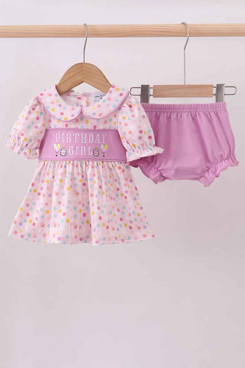 Baby girl's outfit with polka dot dress and pink bloomers on a hanger against a white background